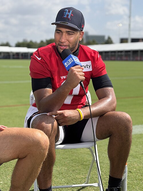 C.J. Stroud speaking into a microphone at Houston Texans training camp in July 2026. Player photograph, not card artwork.