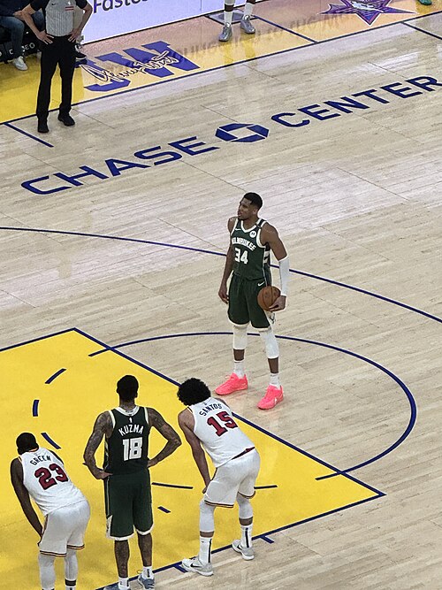 Giannis Antetokounmpo holding a basketball on court in a Bucks uniform in 2025. Player photograph, not card artwork.