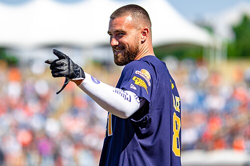 Travis Kelce smiling and pointing at a charity event in 2021. Player photograph, not card artwork.