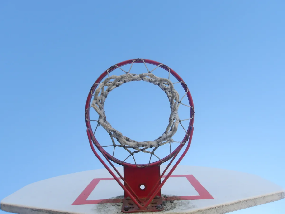 An outdoor basketball hoop viewed from below against a blue sky.