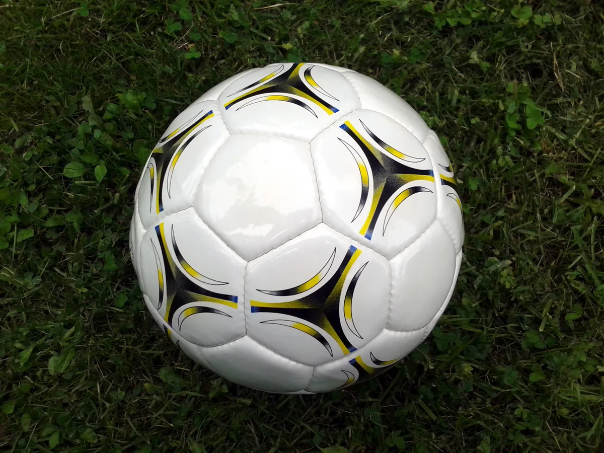 A white soccer ball with black and yellow panels resting on grass.
